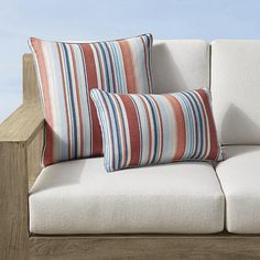 two striped pillows sit on top of a white couch next to a wooden railing and blue sky