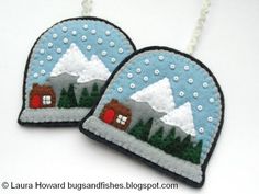 two handmade snow globes with houses and trees on them, hanging from a chain