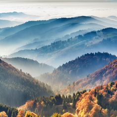 the mountains are covered in colorful trees and foggy skies as they rise into the distance