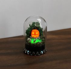 a glass dome with a fake pumpkin in it on a wooden table next to a white wall