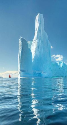 an iceberg floating in the ocean with a red sailboat on it's side