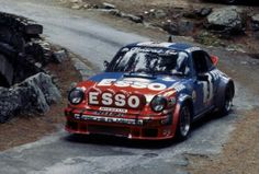 an old race car driving down a road in front of some rocks and dirt with the word esso written on it