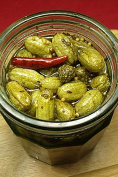 a glass jar filled with pickles on top of a wooden table next to a red pepper