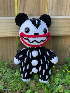 a black and white stuffed animal with a red nose sitting in the grass next to a fence