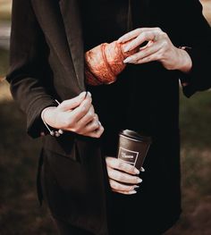 a woman in a black suit holding a cup and a croissant wrapped around her arm