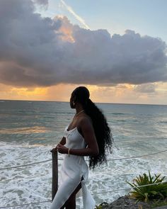 a woman standing on top of a beach next to the ocean under a cloudy sky