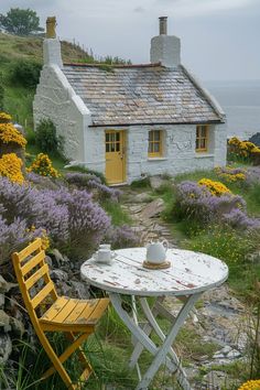 a table and chair sitting in front of a small white house next to the ocean