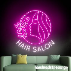 the hair salon neon sign is lit up against a dark wall with a couch and pillows