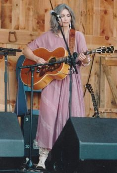 a woman standing in front of a microphone and holding a guitar