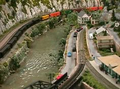 a model train set is shown with cars and trucks on the tracks next to a body of water