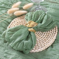 a basket with some green cloth on top of it next to a wine glass and reeds