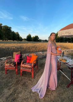 a woman in a long dress standing next to an outdoor table with food on it