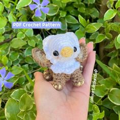 a hand holding a tiny stuffed animal in front of some plants and bluebells