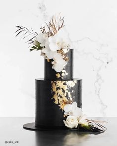 a black and gold wedding cake with white flowers on the top, sitting on a table