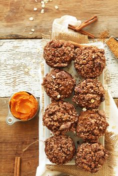 chocolate muffins on a white plate with cinnamon sticks and an orange bowl in the background