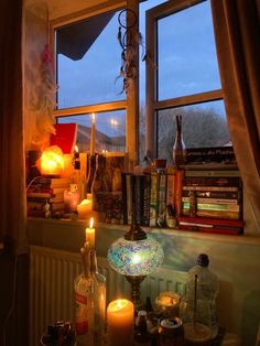 a table with candles, books and bottles on it in front of a large window