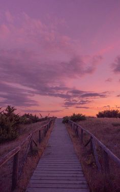 a wooden walkway leading to the beach at sunset with clouds in the sky and grass on either side