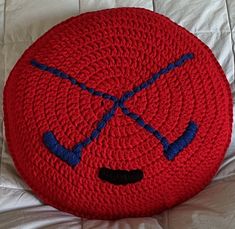 a crocheted red cushion with blue handles and two crossed sticks on the face