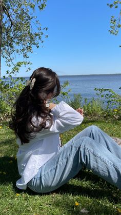 a woman sitting on the grass next to water