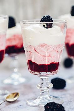 two glasses filled with dessert sitting on top of a table next to berries and spoons