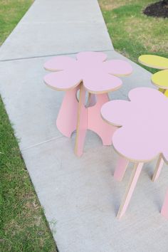 three pink and yellow flower shaped tables sitting on the side of a sidewalk next to grass