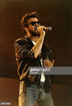 a man with sunglasses and a leather jacket on holding a microphone in his right hand