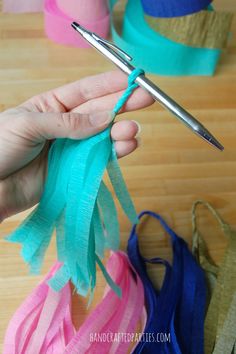 a person is holding scissors and threading something blue, pink, and green with other items in the background