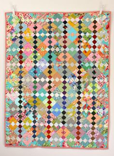 a multicolored quilt hanging on the wall in front of a white wall with an orange frame