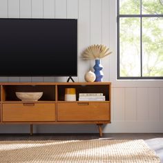 a flat screen tv sitting on top of a wooden entertainment center next to a window