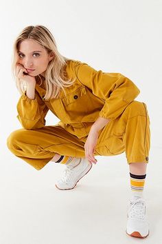 a woman in yellow is posing with her hand on her chin and looking at the camera