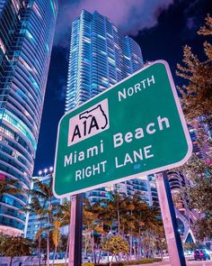 a green street sign sitting in front of tall buildings at night with the words miami beach right lane written on it