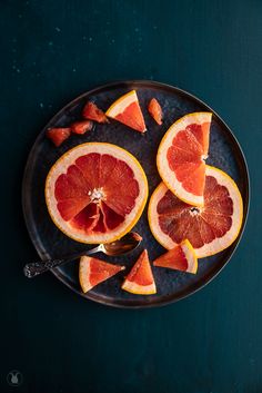 grapefruit cut in half on a black plate with spoons and green background