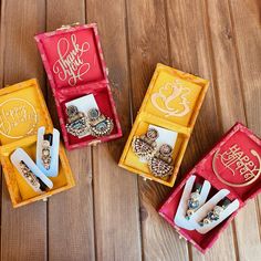 three boxes with different types of jewelry in them on a wooden surface, one containing earrings and the other containing rings