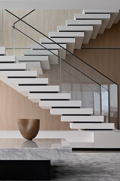 a modern staircase in a house with marble and wood accents on the walls, along with a large vase