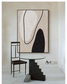 an abstract painting hangs on the wall next to a chair and table