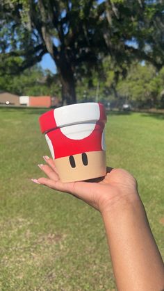 a person holding up a paper cup with a mushroom on it's head in the grass