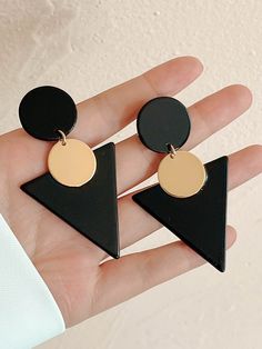 the black and gold triangle earrings are on someone's hand