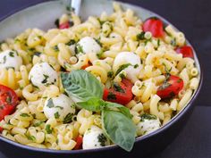 a pasta salad with tomatoes, mozzarella and spinach in a black bowl