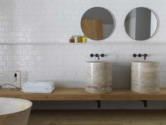 two round mirrors on the wall in a white tiled bathroom with wood countertop and bathtub