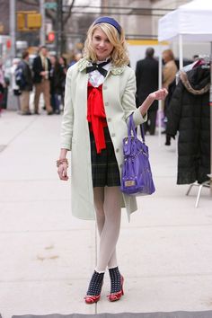 a woman is standing on the sidewalk with her hand in her pocket and holding a purple purse