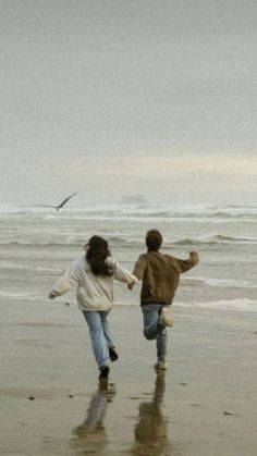 two people running on the beach holding hands