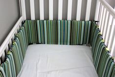 a baby crib with a white sheet and striped bedding on the bottom half