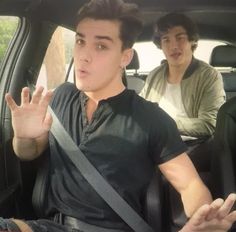 two young men sitting in the back seat of a car, one holding his hand up