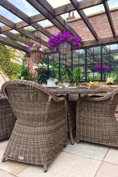 Traditional, elegant rattan dining set dressed with rattan placemats, bowls and wine glasses. Bright flower baskets hang from an overhead pergola. Outdoor Ottoman