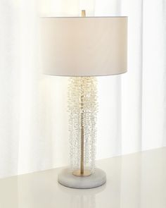 a lamp on a table in front of a window with white drapes and curtains