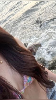 a woman sitting on the beach with her hair blowing in the wind and water behind her