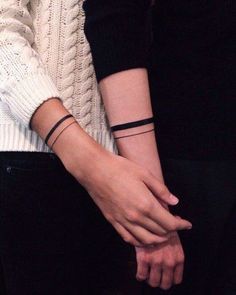 two people holding hands with one wearing a bracelet and the other in a black shirt