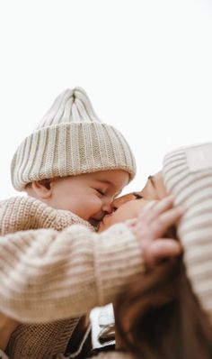 a woman holding a baby in her arms while wearing a knitted hat and sweater