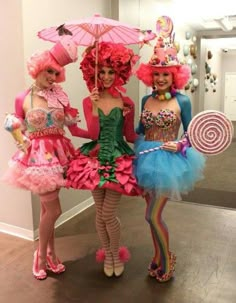 three women dressed up in costumes holding umbrellas and lollipops are standing next to each other