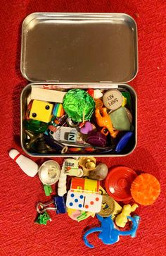 an open tin box filled with toys on a red blanket next to a toy elephant